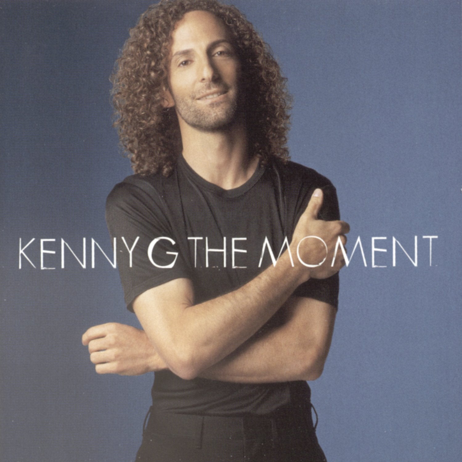 Album cover with a person crossing arms and text 'Kenny G The Moment' on a blue background